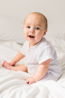 Evdeki beyaz yatakta gülümseyen yeni doğmuş bebek, sağlıklı bebek konsepti. Alfa ve alfa jenerasyonu..
