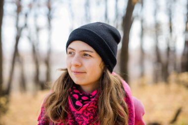 Güz parkında poz veren uzun saçlı, siyah şapkalı ve pembe ceketli güzel, mutlu bir kız. Açık hava portresi gün ışığı. Sonbahar moda konsepti. Metin için boş alanı kopyala.