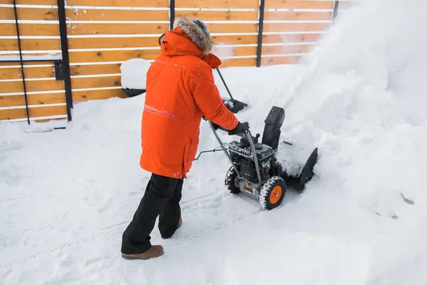 A man clear snow from backyard with snow blower. Winter season and snow blower equipment.