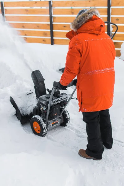 A man clear snow from backyard with snow blower. Winter season and snow blower equipment.