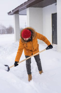 Bir adam soğuk bir günde evin önündeki karları temizler ve temizler. Kış günü sokakları kardan temizlemek. Kışın şiddetli kar yağışı ve şiddetli kar fırtınası