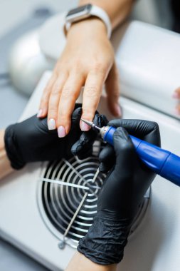 Kadın usta kuaförde manikür yaparken elektrikli tırnak törpüsü kullanıyor..