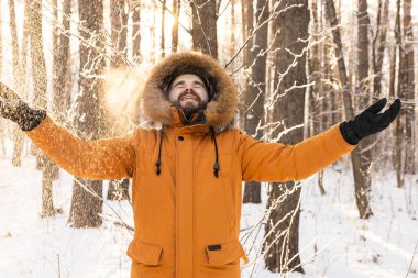 Happy bearded man in hat throws up snow in winter nature. Snowy cold season and holidays lifestyle