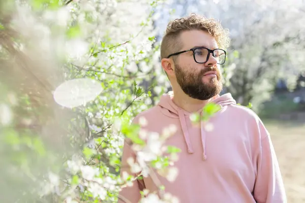 Cool handsome millennial man side face looking away portrait in blooming springtime trees. Blur sakura blossom spring tree background. Copy space.