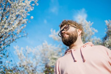Bahar bahçesindeki çiçek açan badem ya da kiraz ağacıyla dalların altında duran erkek sakallı adam. Bahar çiçeği. Boşluğu kopyala