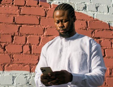 Afrika kökenli Amerikalı şık etnik Dashiki 'li bir adam açık havada boş zamanların tadını çıkarırken sosyal ağlarda fotoğraf çektiriyor. Koyu tenli adam akıllı telefondan ve sosyal ağlardan komik videolar izliyor.