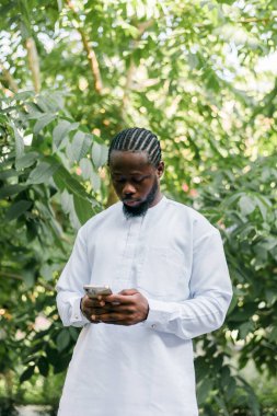 Kültürel ve etnik kıyafetleri olan Afrikalı Amerikalı hippi dışarıda akıllı telefondan sohbet ediyor sosyal ağlarda arkadaşlarıyla mesajlaşıyor. Milenyum ve İnternet kavramı.