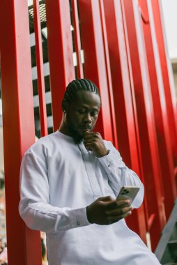 Afrika kökenli Amerikalı şık etnik Dashiki 'li bir adam açık havada boş zamanların tadını çıkarırken sosyal ağlarda fotoğraf çektiriyor. Koyu tenli adam akıllı telefondan ve sosyal ağlardan komik videolar izliyor.