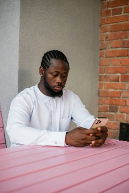 Afrika kökenli Amerikalı şık etnik Dashiki 'li bir adam açık havada boş zamanların tadını çıkarırken sosyal ağlarda fotoğraf çektiriyor. Koyu tenli adam akıllı telefondan ve sosyal ağlardan komik videolar izliyor.