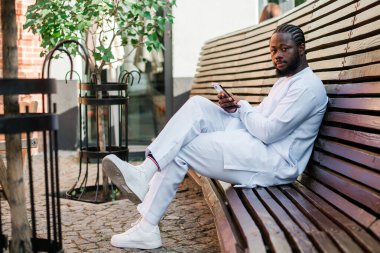 Afrika kökenli Amerikalı şık etnik Dashiki 'li bir adam açık havada boş zamanların tadını çıkarırken sosyal ağlarda fotoğraf çektiriyor. Koyu tenli adam akıllı telefondan ve sosyal ağlardan komik videolar izliyor.