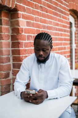 Afrikalı Amerikalı yaz günü sokak kafesinde cep telefonlarını kontrol eder. Milenyum jenerasyonu ve Z jenerasyonu insanları. Sosyal ağlar ve randevu uygulaması