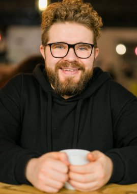 Kafede şık gözlükler takan genç ve serbest çalışan bir adamın yakın portresi. Kameraya, eğitime ve online çalışma konseptine bakan kendine güvenen mutlu öğrenci. Y jenerasyonu ve Y jenerasyonu
