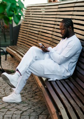 Milenyum kuşağı Afro-Amerikan erkeği açık havada internet konsepti yazıyormuş. Telefonda yüksek hızlı internet, sosyal ağlarda sohbet ve blog