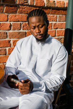 Afrika kökenli Amerikalı şık etnik Dashiki 'li bir adam açık havada boş zamanların tadını çıkarırken sosyal ağlarda fotoğraf çektiriyor. Koyu tenli adam akıllı telefondan ve sosyal ağlardan komik videolar izliyor.