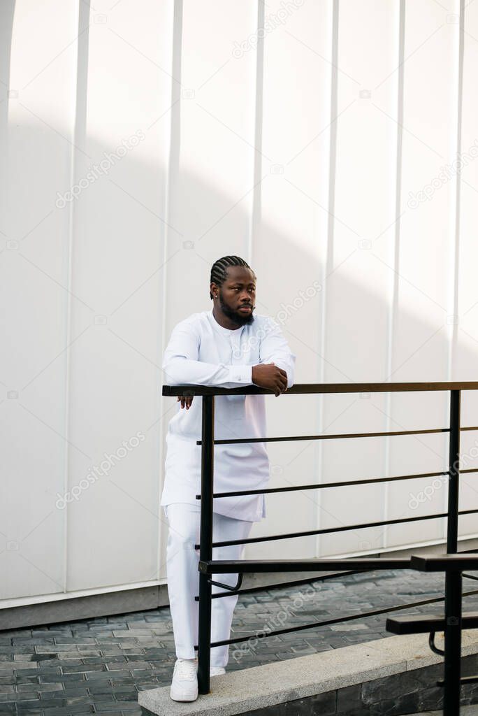 Cheerful male tourist dress in white wear dashiki ethnic smiling at city street on stairs. African American travel model have free time.