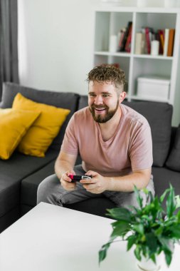 Evdeki kanepede oturmuş video oyunları oynayan neşeli genç adam. Oyun bağımlılığı ve eğlence.