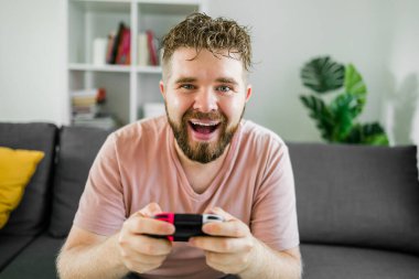 Evdeki kanepede oturmuş video oyunları oynayan neşeli genç adam. Oyun bağımlılığı ve eğlence.