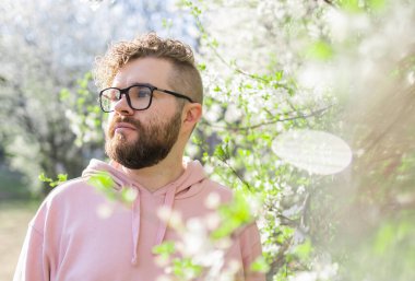 Havalı yakışıklı milenyum erkeği yüzü ilkbahar ağaçlarında portreden uzağa bakıyor. Bulanık sakura çiçeği bahar ağacı arka planı. Boşluğu kopyala.