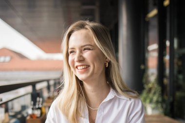 Balkon kafeteryasında gülen güzel sarışın kadının portresi. Gülümseyen mutlu bir kadın kahve dükkanında dinleniyor.