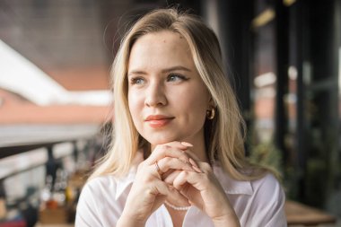 Balkon kafeteryasında çay içen güzel sarışın kadının portresi. Gülümseyen mutlu bir kadın kahve dükkanında dinleniyor.