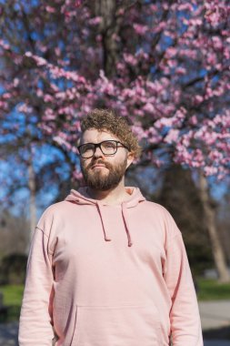 Alerjisi olan bir adam bahar mevsimsel alerjisinden zevk alıyor. Baharda çiçek açan ağacın önünde gülümseyen mutlu sakallı adamın portresi. Bahar çiçekleri ve alerji konsepti. Boşluğu kopyala.