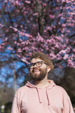 Alerjisi olan bir adam bahar mevsimsel alerjisinden zevk alıyor. Baharda çiçek açan ağacın önünde gülümseyen mutlu sakallı adamın portresi. Bahar çiçekleri ve alerji konsepti. Boşluğu kopyala.