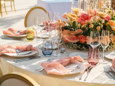 Düğün. Ziyafet. Konuklar, yuvarlak masa ve sandalyeler çatal bıçak takımı, çiçekler ve çanak çömlek ile servis ve bir masa örtüsü ile kaplı