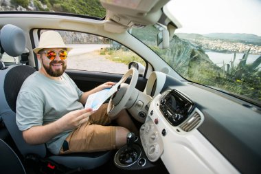 Hippi adam arabadaki konum haritasına bakıyor, turist gezgini sürüyor ve erkeklerin elinde tutuyor Avrupa haritası, manzarası ve planı turist yolu, ulaşım aracıyla yolculuk