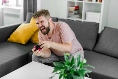 Oturma odasında video oyunu oynayan adam kanepede oturuyor.