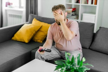 Evdeki kanepede oturmuş video oyunları oynayan neşeli genç adam. Oyun bağımlılığı ve eğlence.