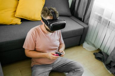 Genç adam evinde oturuyor, evdeki bir kanepede oturuyor ve konsolda oyun oynuyor. Sokak yarışı simülatörü oynamak için kontrolör kullanan bir erkek