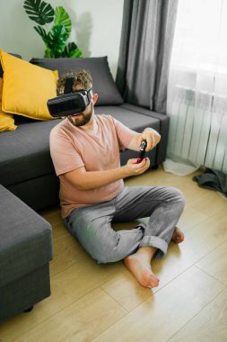 Oturma odasında video oyunu oynayan adam kanepede oturuyor.