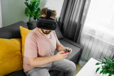 Oturma odasında video oyunu oynayan adam kanepede oturuyor.