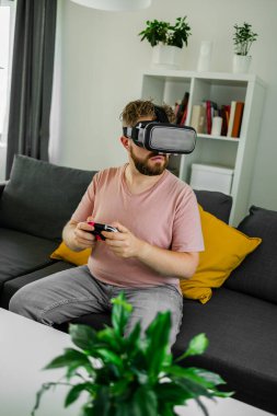 Oturma odasında video oyunu oynayan adam kanepede oturuyor.