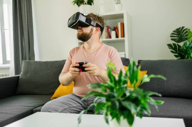 Oturma odasında video oyunu oynayan adam kanepede oturuyor.