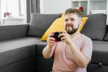 Evdeki kanepede oturmuş video oyunları oynayan neşeli genç adam. Oyun bağımlılığı ve eğlence.