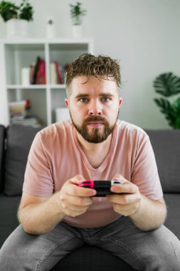 Oturma odasında video oyunu oynayan adam kanepede oturuyor.