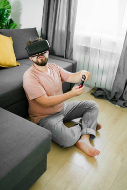 Genç adam evinde oturuyor, evdeki bir kanepede oturuyor ve konsolda oyun oynuyor. Sokak yarışı simülatörü oynamak için kontrolör kullanan bir erkek