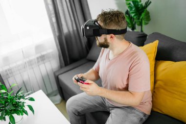 Oturma odasında video oyunu oynayan adam kanepede oturuyor.