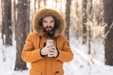 Close-up portrait handsome bearded millennial man in winter clothes and with thermos snow outdoor. Cold season and hot beverage in winter time.