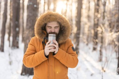 Close-up portrait handsome bearded millennial man in winter clothes and with thermos snow outdoor. Cold season and hot beverage in winter time.