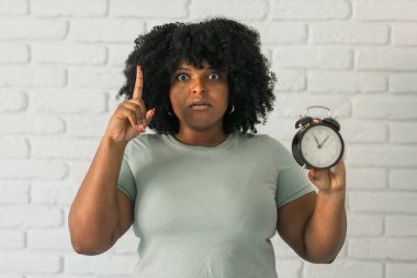 Şaşırmış Afro-Amerikalı kadın elinde çalar saat tutarken ağzı açık kalmış ve evinde, tuğladan arka planda mutlu bir yüz görmüş. Geç kalmak ve zaman çabucak geçiyor.