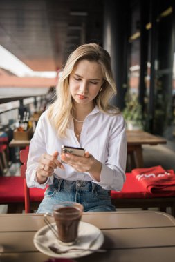 Restoran ve akıllı telefon. Sarışın, yazı yazan, kaydıran ya da e-postayı kontrol eden ya da sosyal medya uygulaması ya da sosyal ağ kullanıcısı ile iletişime geçen bir kadın. Mutlu bir gülümseme ve gezici teknolojisi olan genç bir kız.