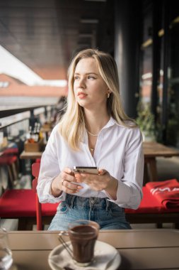 Restoran ve akıllı telefon. Sarışın, yazı yazan, kaydıran ya da e-postayı kontrol eden ya da sosyal medya uygulaması ya da sosyal ağ kullanıcısı ile iletişime geçen bir kadın. Mutlu bir gülümseme ve gezici teknolojisi olan genç bir kız.