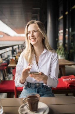 Restoran ve akıllı telefon. Sarışın, yazı yazan, kaydıran ya da e-postayı kontrol eden ya da sosyal medya uygulaması ya da sosyal ağ kullanıcısı ile iletişime geçen bir kadın. Mutlu bir gülümseme ve gezici teknolojisi olan genç bir kız.