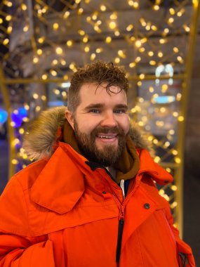 Kış kırmızı ceketli, saç stili olan yakışıklı milenyum erkek mankeni, gece şehirde şenlikli ışıklarla yürüyor. Noel ve kış tatilleri.