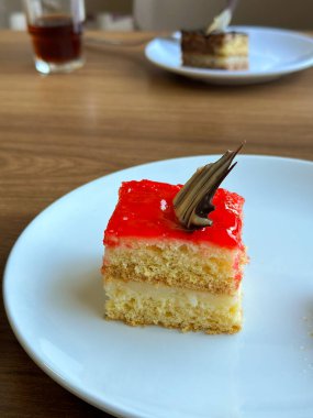 Parlak kırmızı kaplamalı lezzetli bir dilim pasta beyaz bir tabakta zarif bir şekilde duruyor. Hoşgörü ve zevk kavramı. Tatlı ve şeker