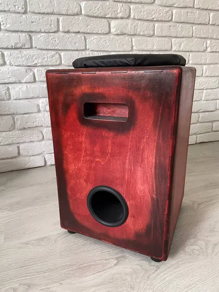 stock image Cajon drum sits elegantly against a textured white brick wall, highlighting its wooden craftsmanship. Musical Instrument for creating music at home and hobby concept.