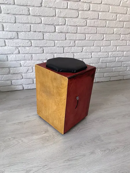 stock image Cajon drum sits elegantly against a textured white brick wall, highlighting its wooden craftsmanship. Musical Instrument for creating music at home and hobby concept.