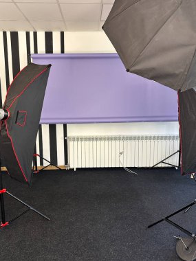 Profesyonel fotoğraf stüdyosu, ışıklandırma ekipmanları ve mor bir arka plan. Stüdyo iyi donanımlı ve fotoğraf çekimi ya da video kaydı için hazır..